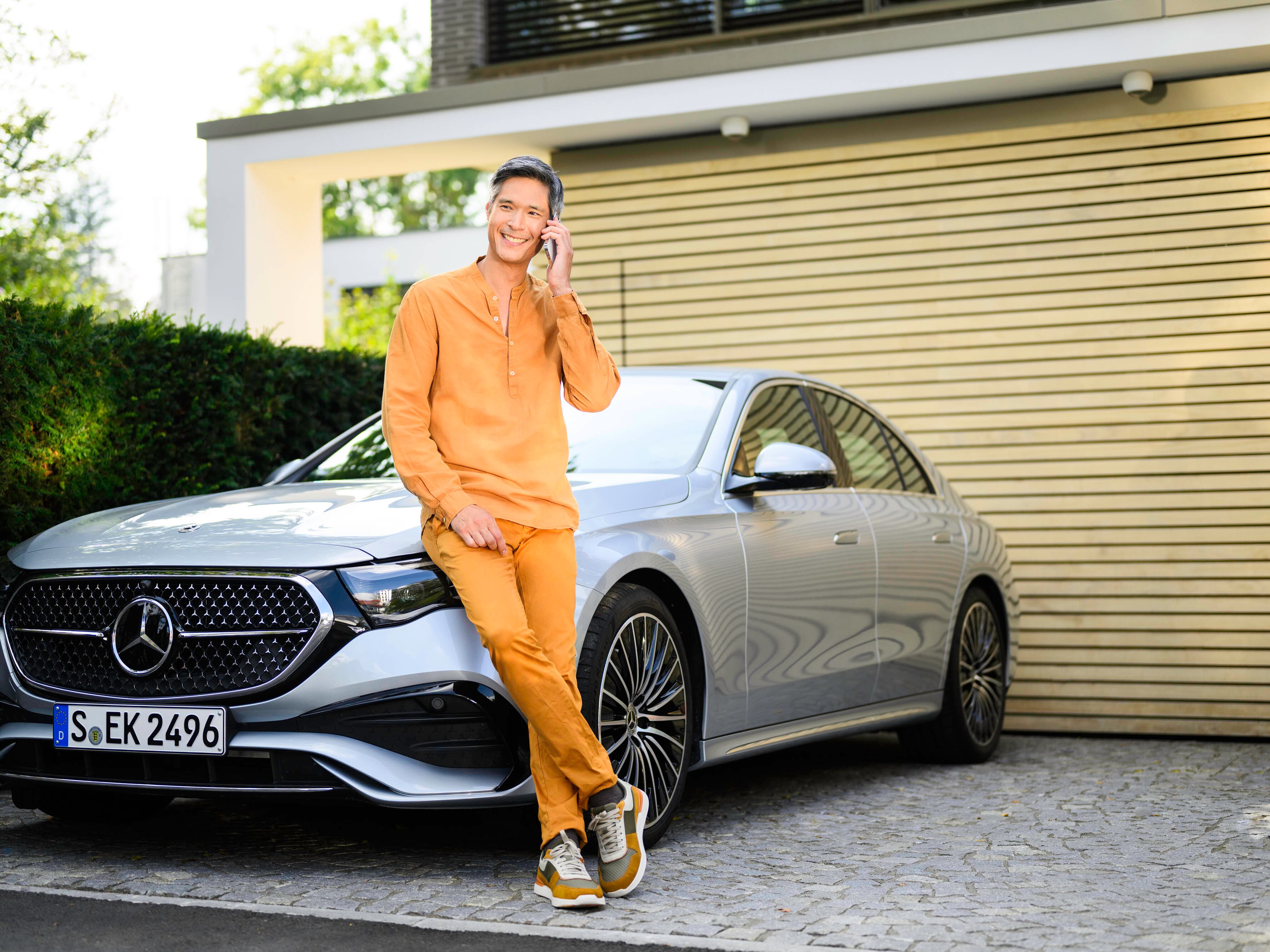 A person leaning against a Mercedes-Benz vehicle, looking at the camera and using a mobile device.