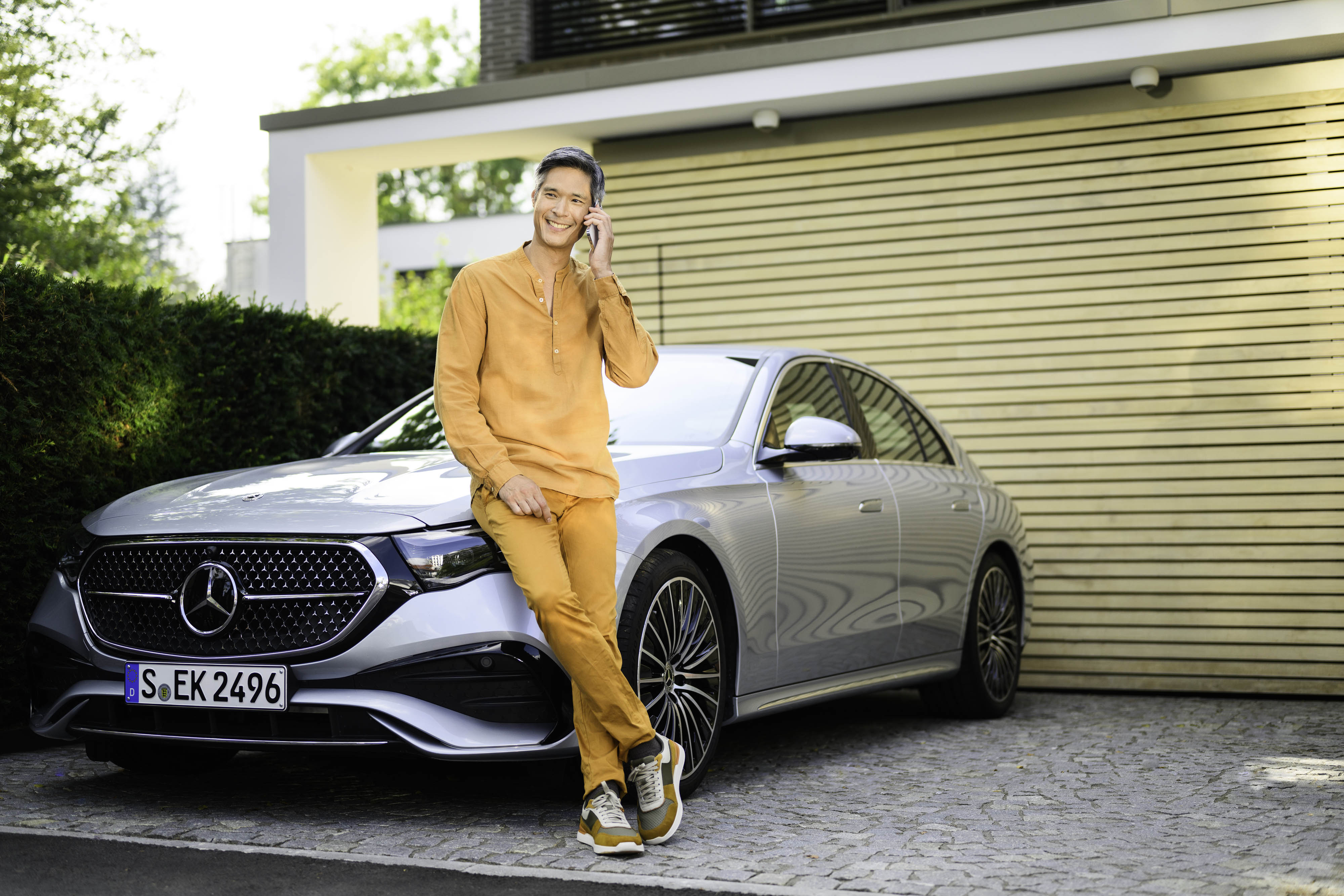 Get a quote for your Mercedes-Benz motor insurance A person leaning against a Mercedes-Benz vehicle, looking at the camera and using a mobile device.