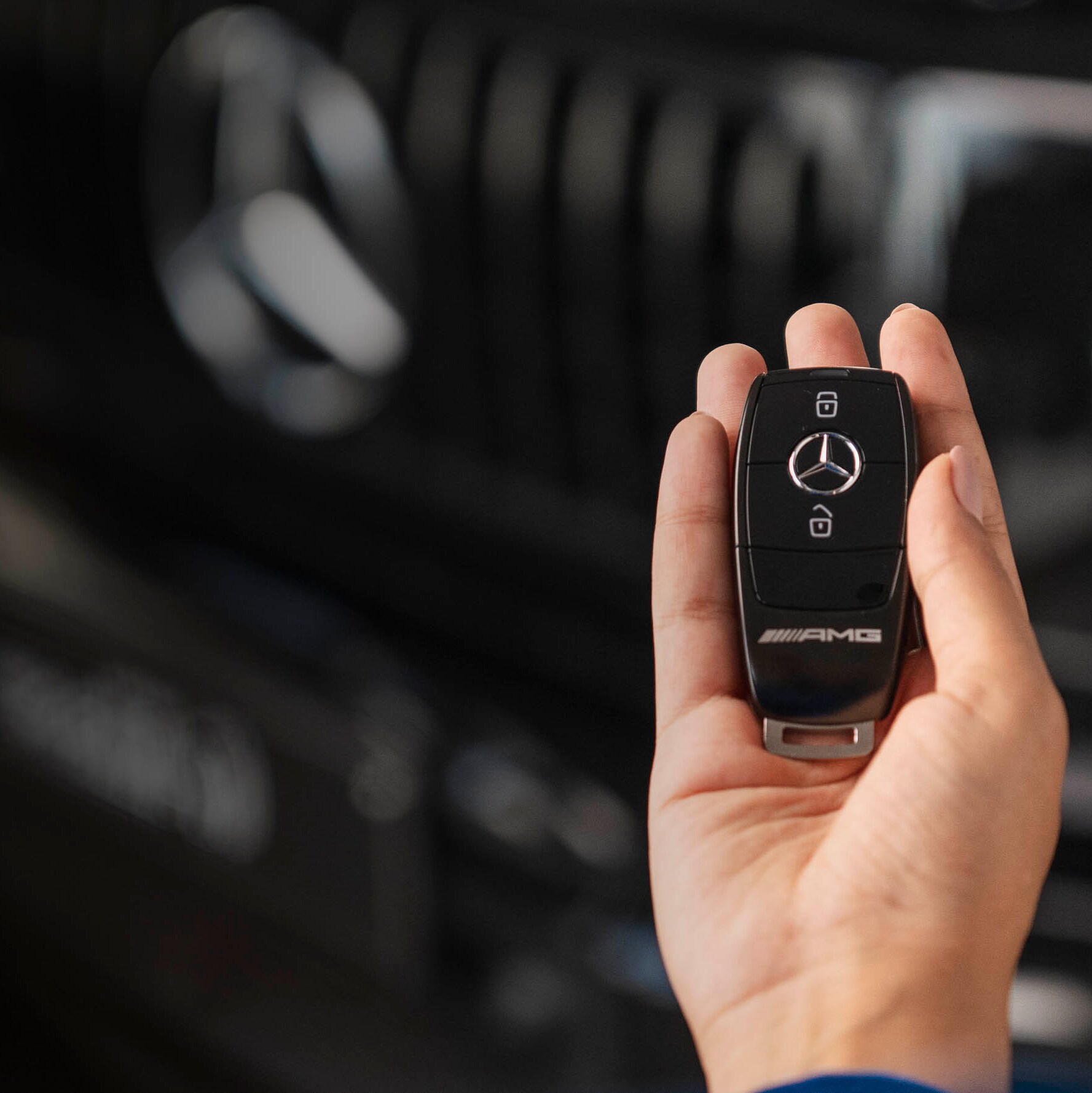A person holding a Mercedes-Benz car key and in front of a Mercedes-Benz vehicle.