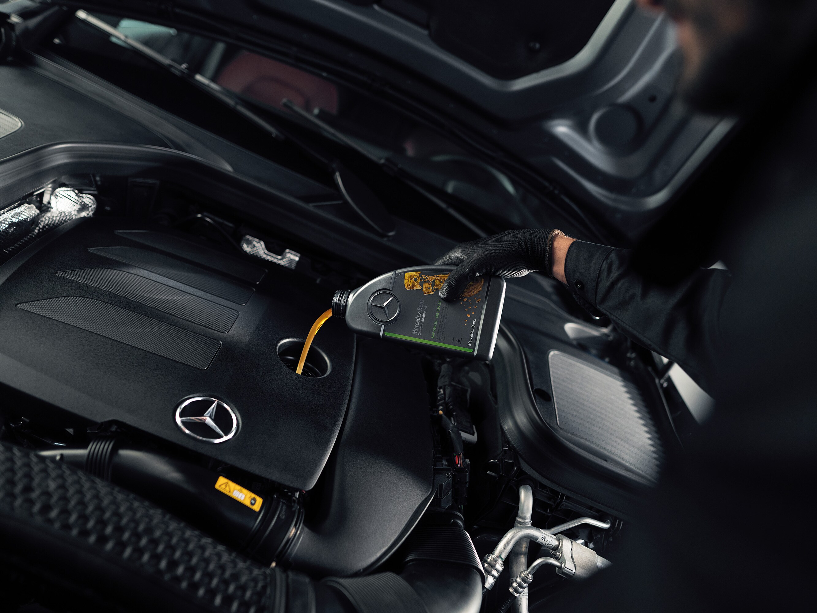 A person pouring engine oil into the Mercedes-Benz vehicle.