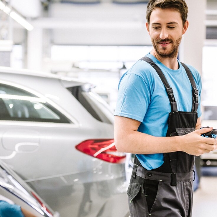 Woman standing in front of her Mercedes-Benz with her phone in her hand and being in a call