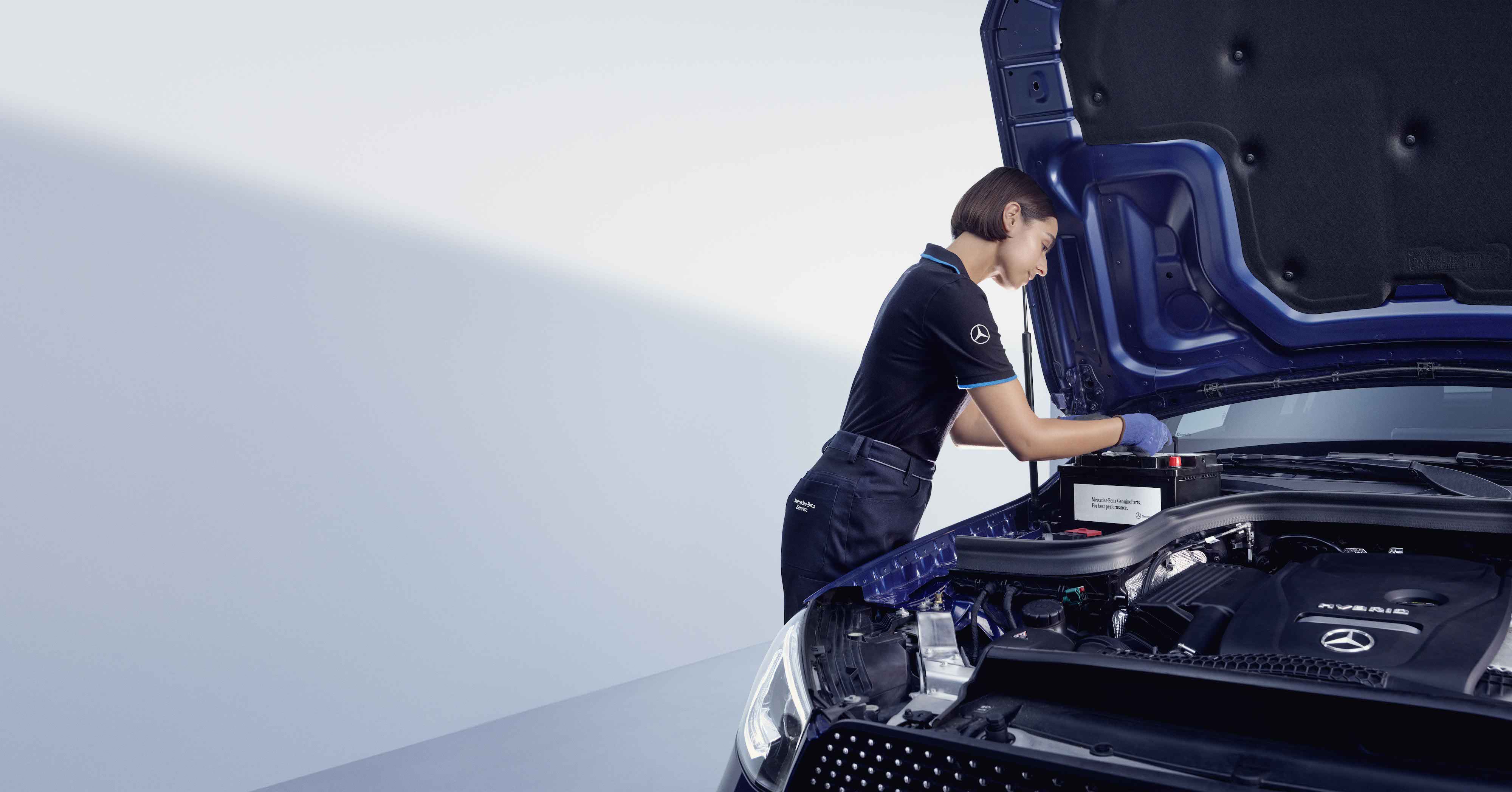A automotive mechanic bends over the open bonnet of a Mercedes-Benz. Genuine Parts | Mercedes-Benz