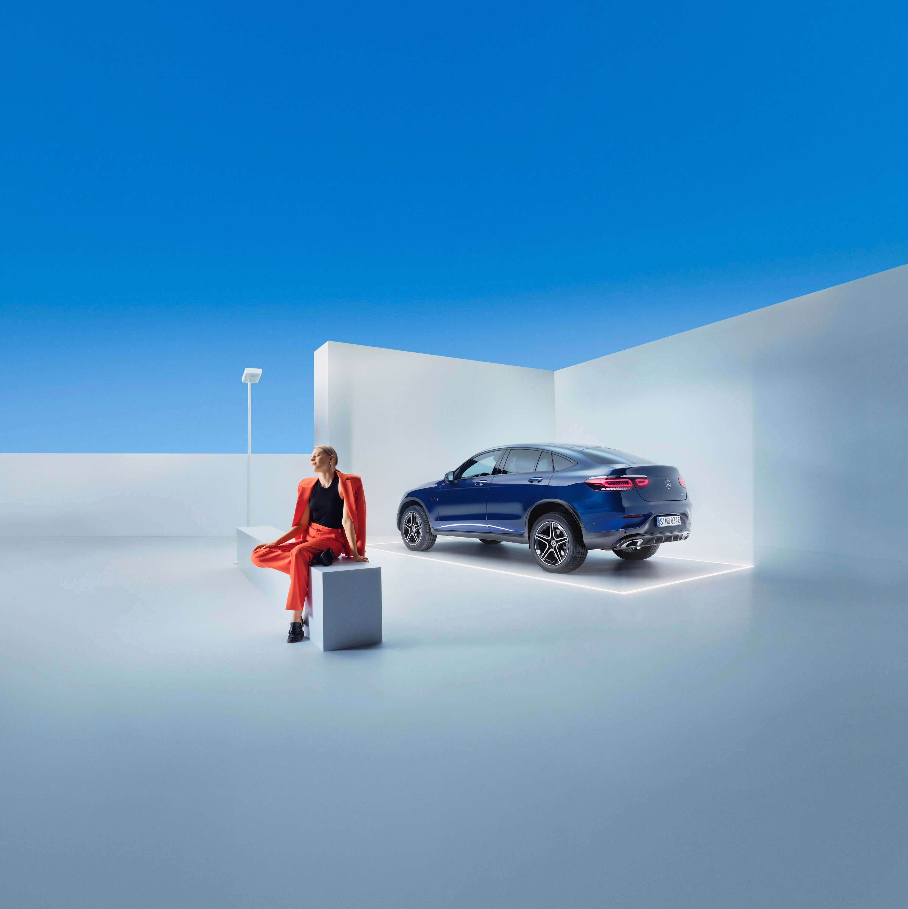 A woman is sitting on a bench in front of a Mercedes-Benz.
