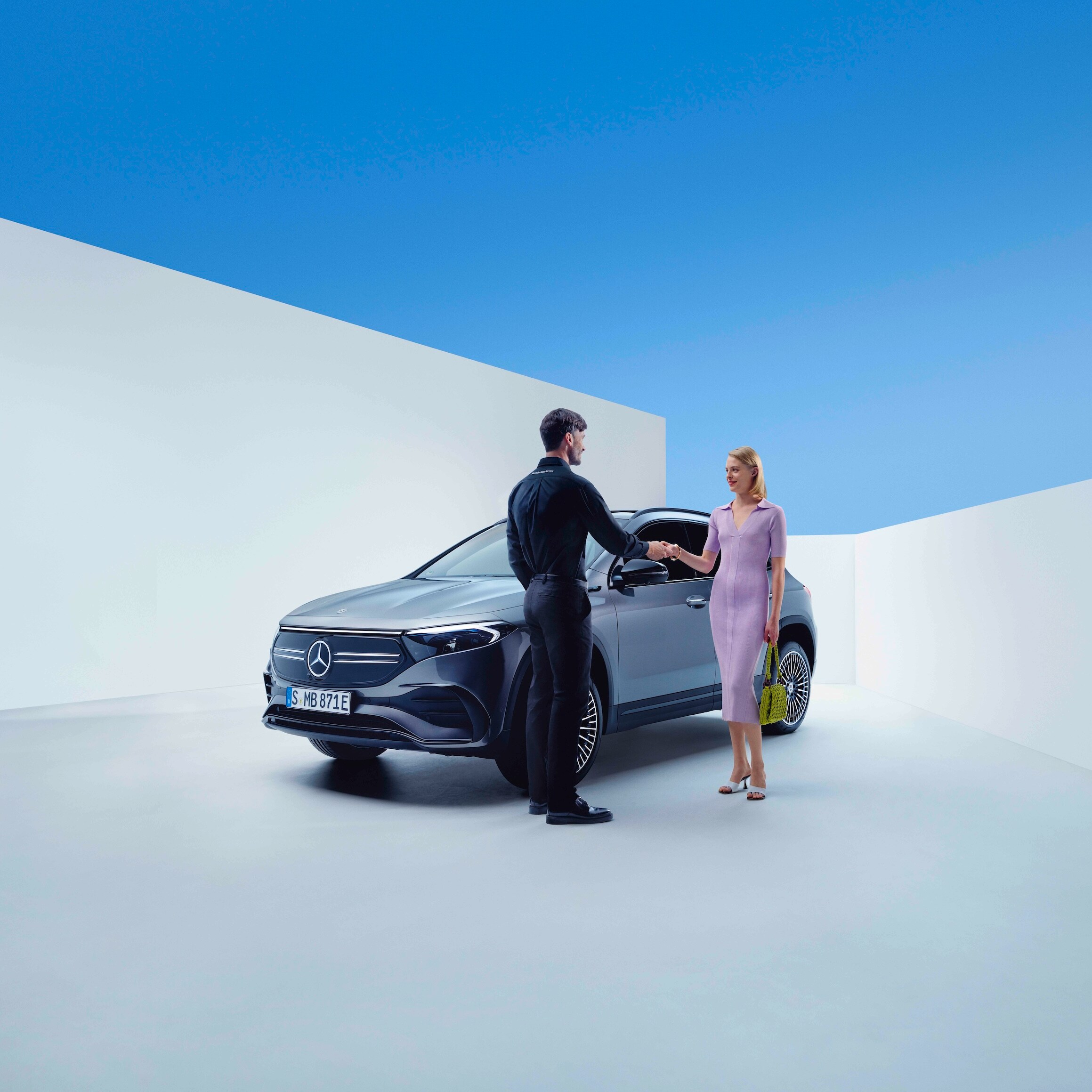 A Mercedes-Benz employee and a woman are shaking hands in front of a Mercedes-Benz