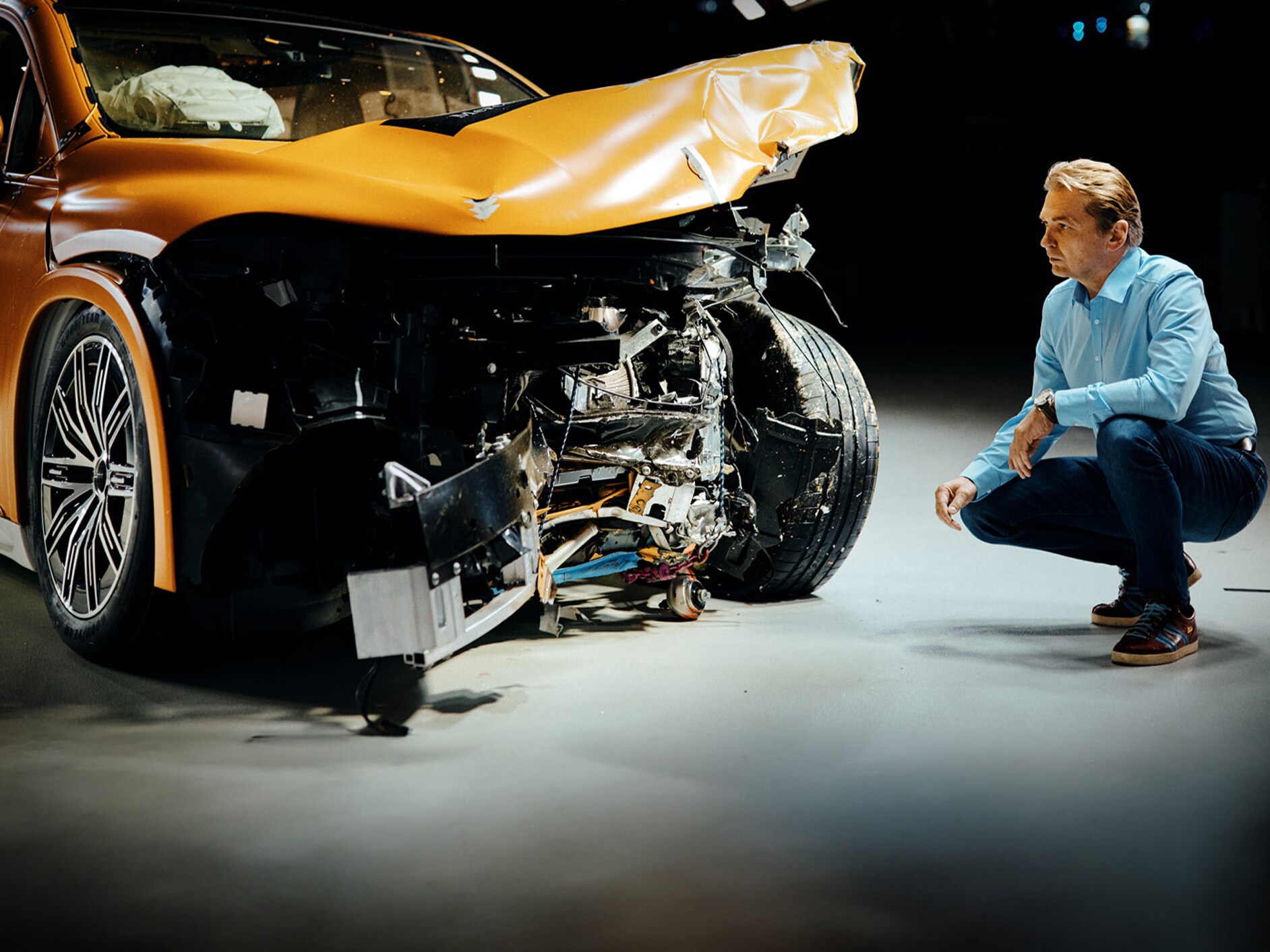 Crash test expert examing front-crashed Mercedes-Benz car while crouching bedite it.