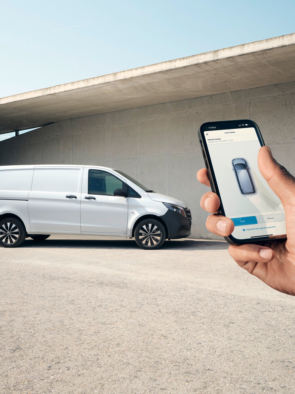 Hand holding up a smartphone showing the Mercedes me App. Vito panel van in the background.