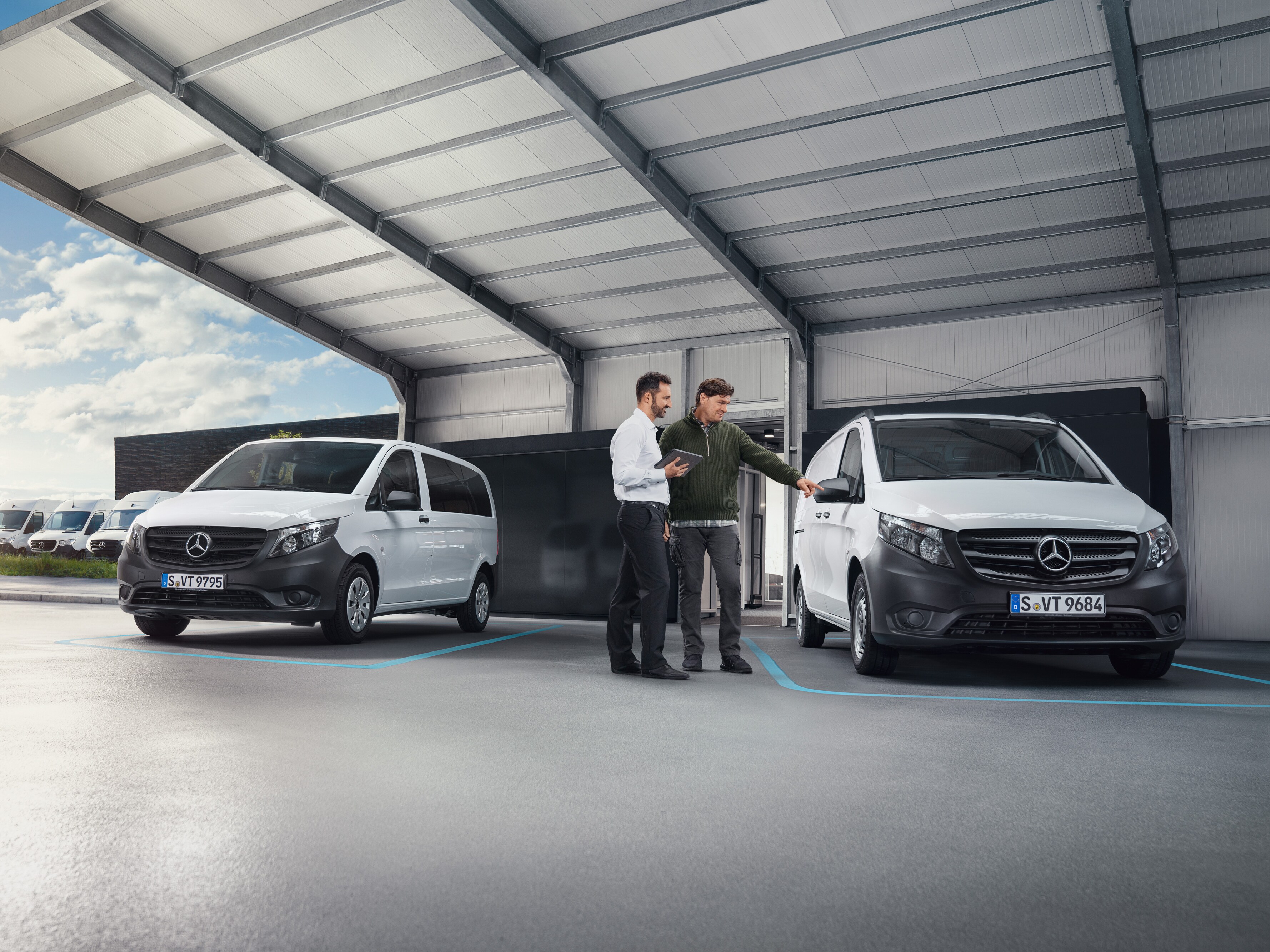 Two people talking in a worksop standing in front of two white Mercedes-Benz vans.