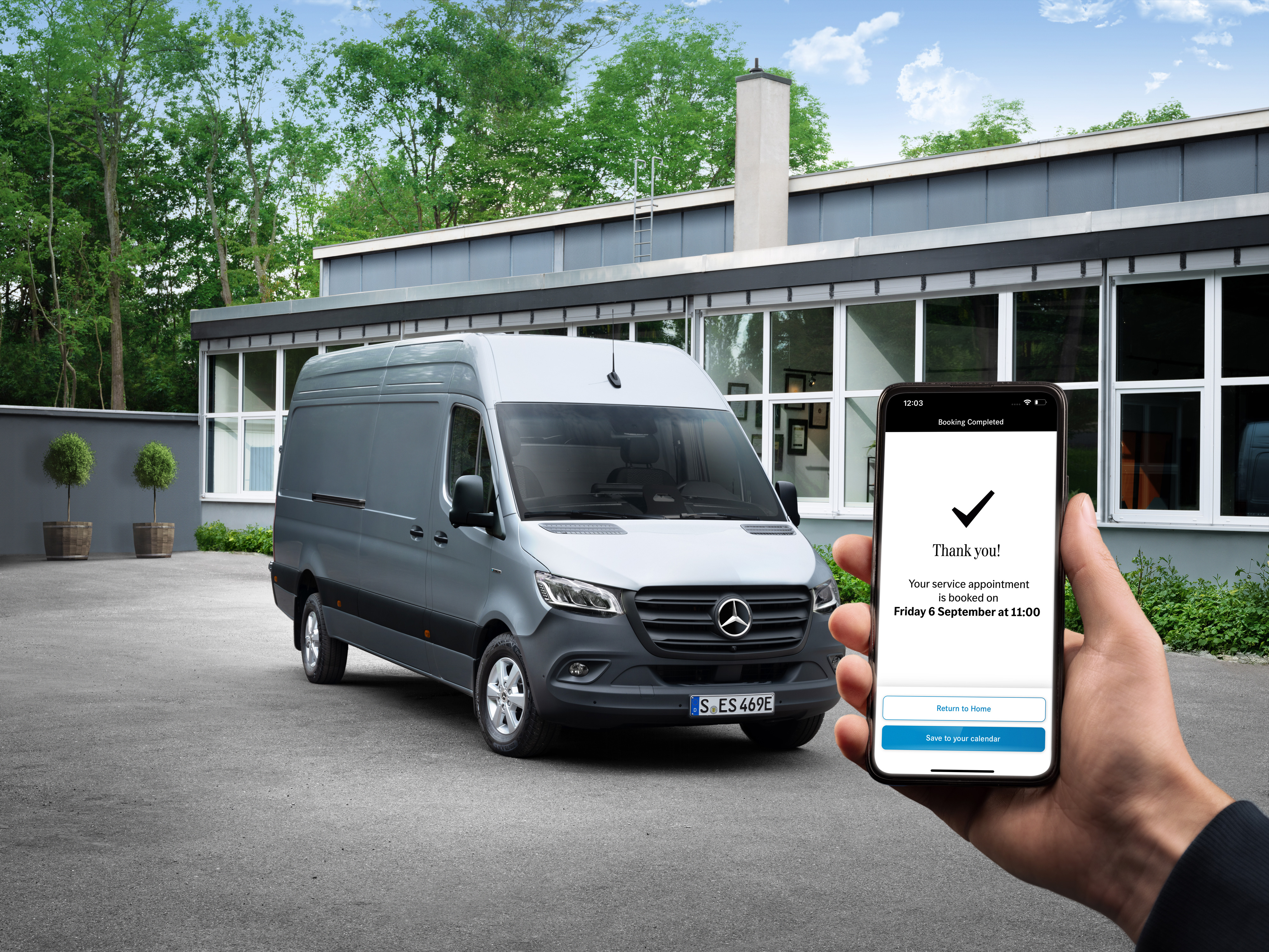 Mercedes-Benz | 便利 | 服務合作夥伴 一輛灰色的 Mercedes-Benz Sprinter 小型商用車在辦公室前,前景中有一個人拿著智能手機。