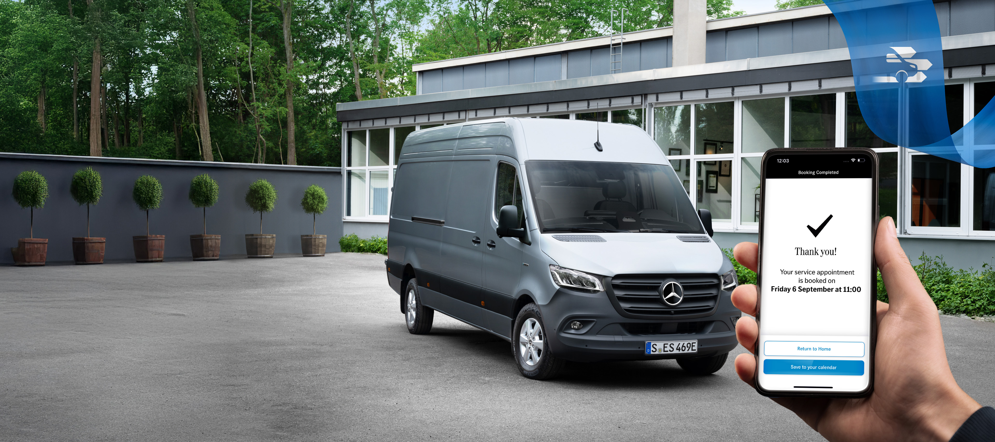 Mercedes Benz | 便利 | 線上預約 一輛灰色的 Mercedes-Benz Sprinter 小型商用車在辦公大樓前,手持智能手機在前景中。