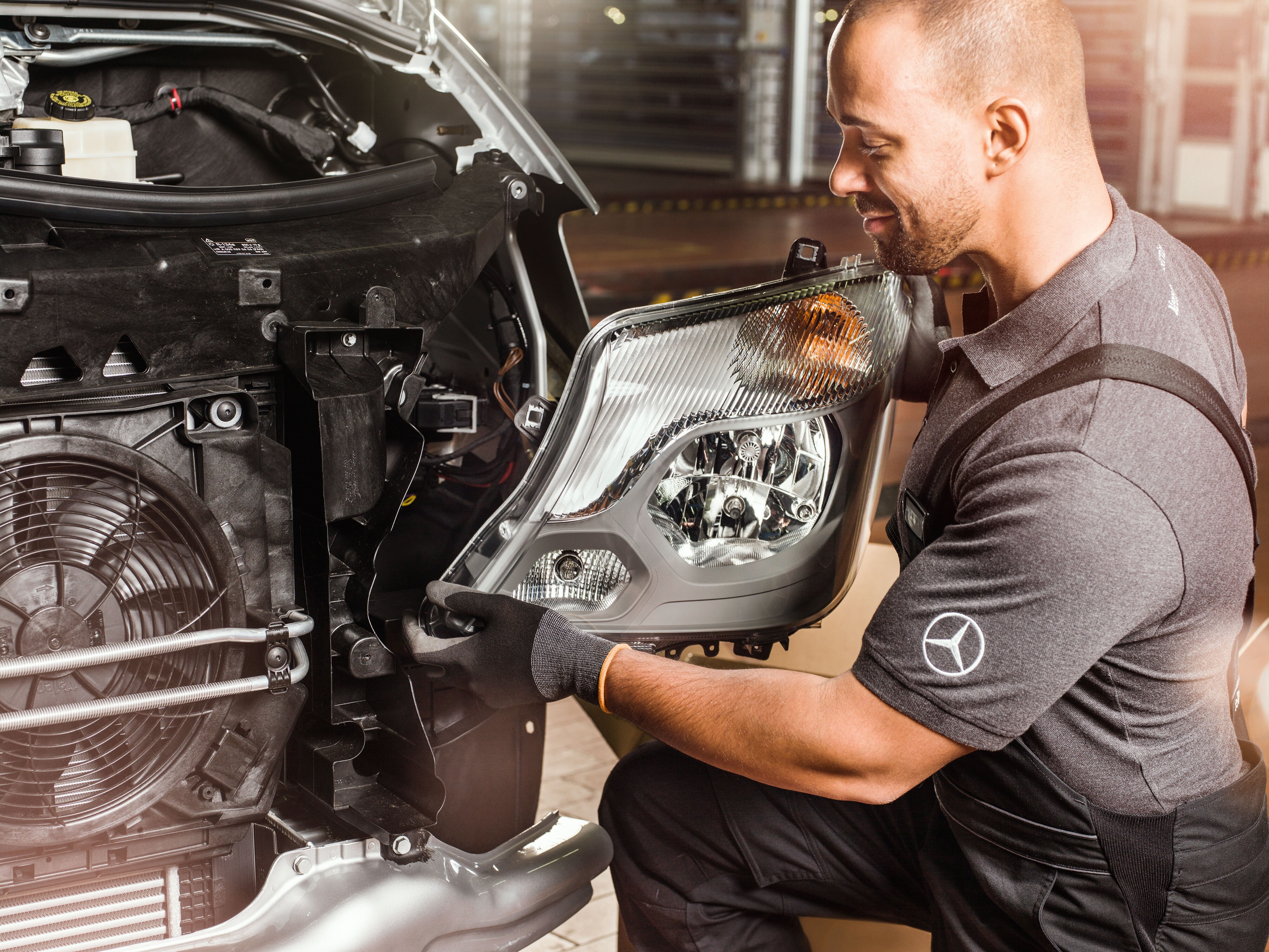 Mechanic checking Mercedes-Benz Genuine Parts in front of an open Sprinter engine, matching the Mercedes spare parts catalogue. 