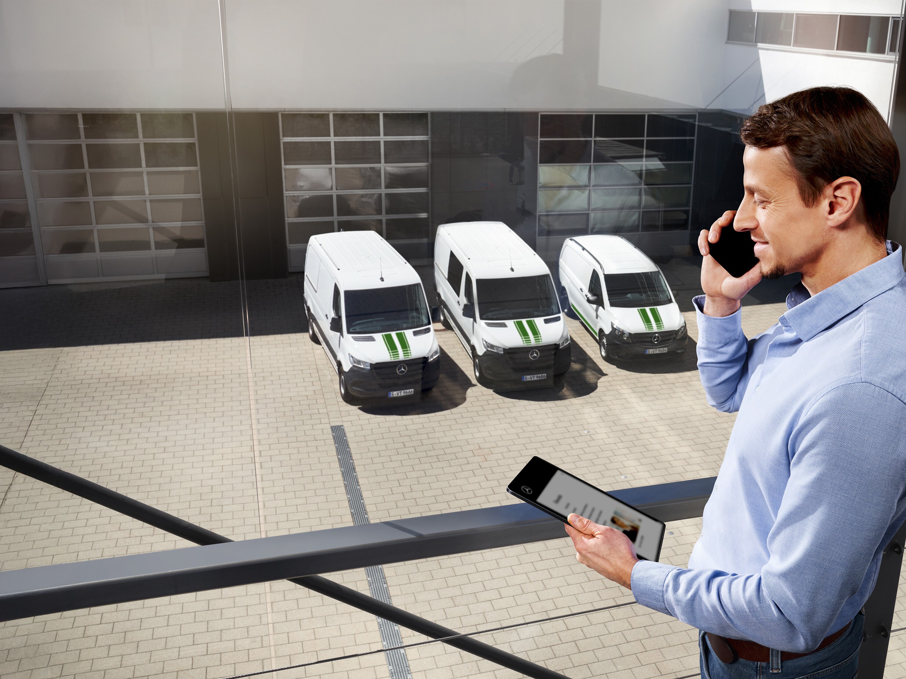 Man on the phone with tablet in front of three Mercedes-Benz vans, topic: how long is the manufacturer’s warranty at Mercedes-Benz?
