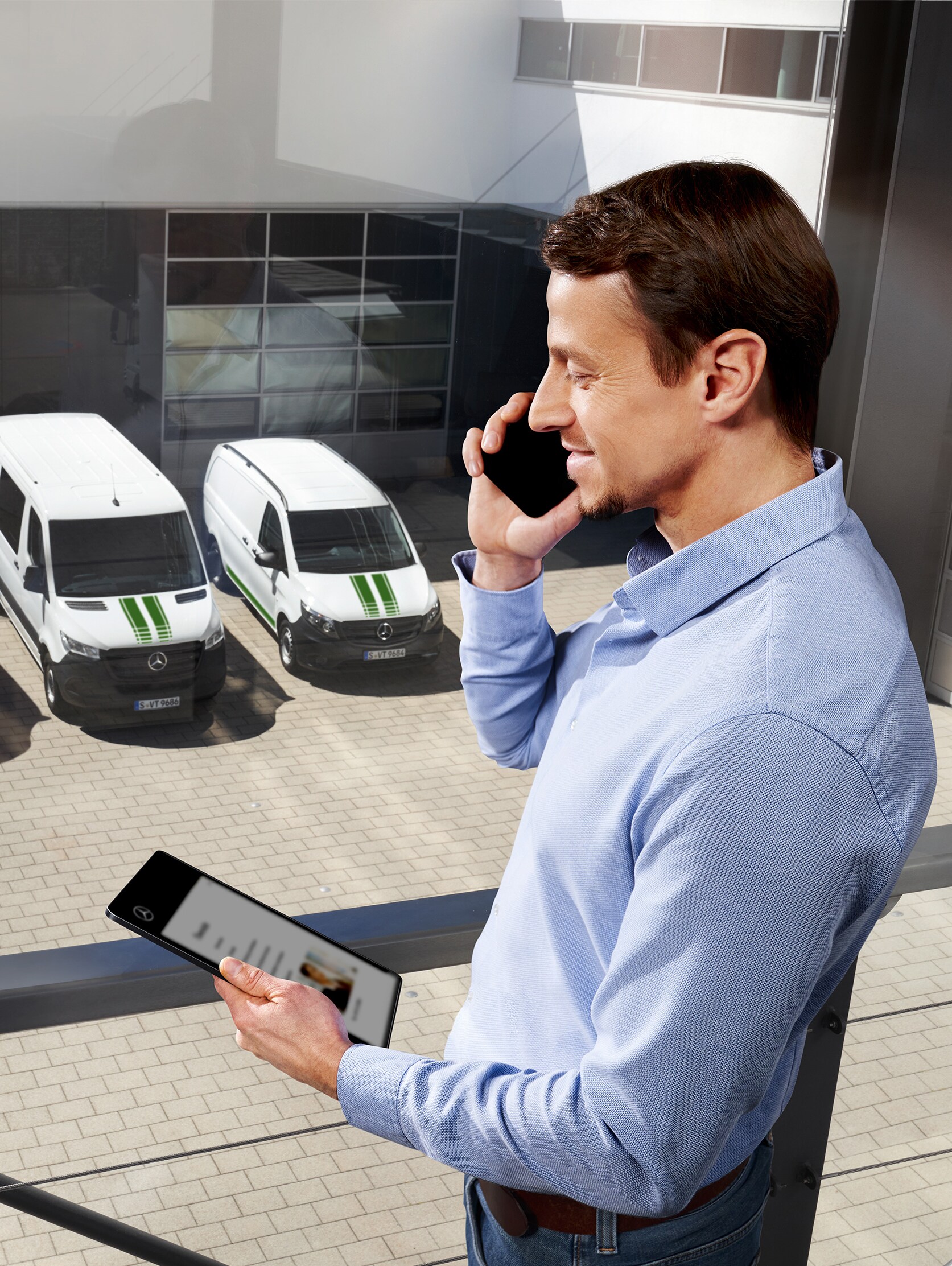 Man with tablet and mobile phone in front of three Mercedes-Benz vans, symbolising quality and reliability of the Mercedes-Benz calibre.