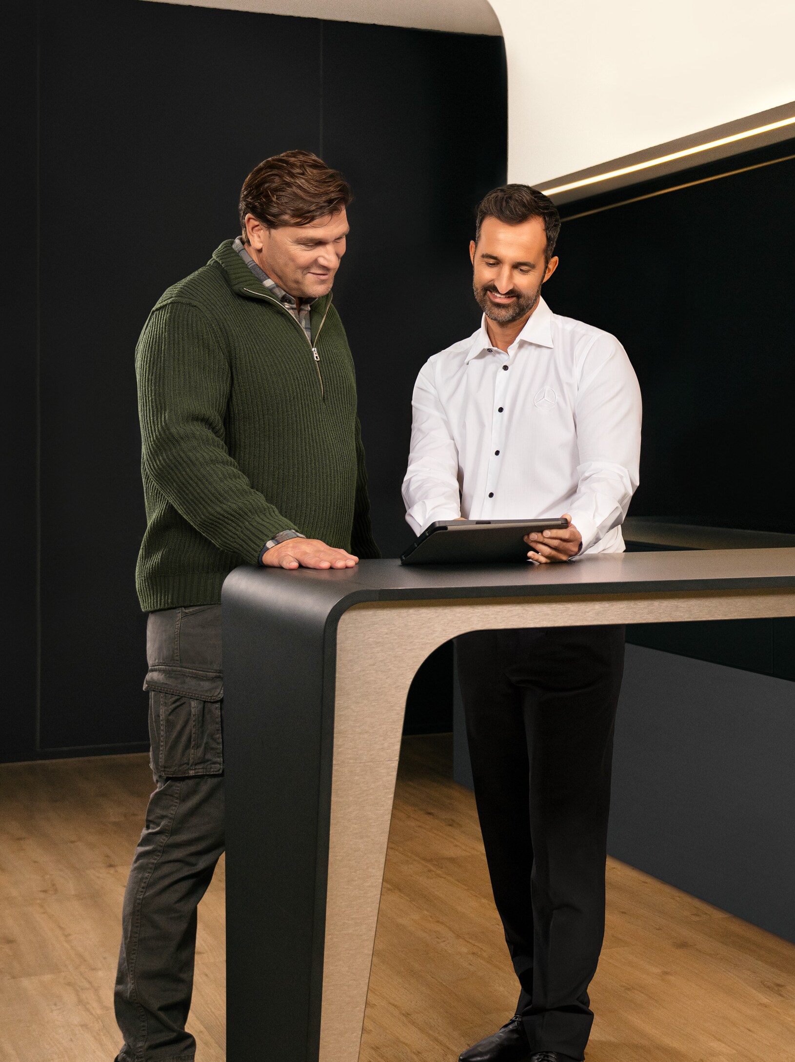 Two men having a consultation standing around a table looking at an iPad.