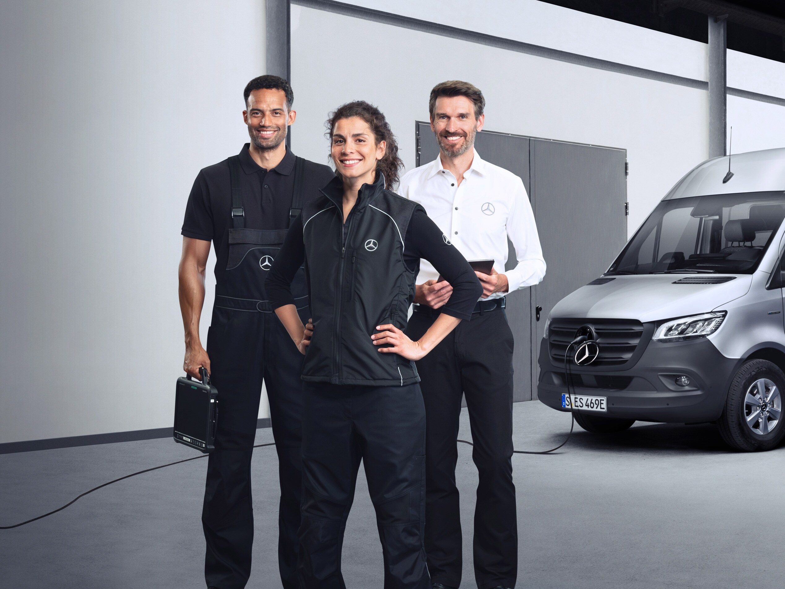 Three employees standing in front of a silver Mercedes-Benz eSprinter with charging cable attached.