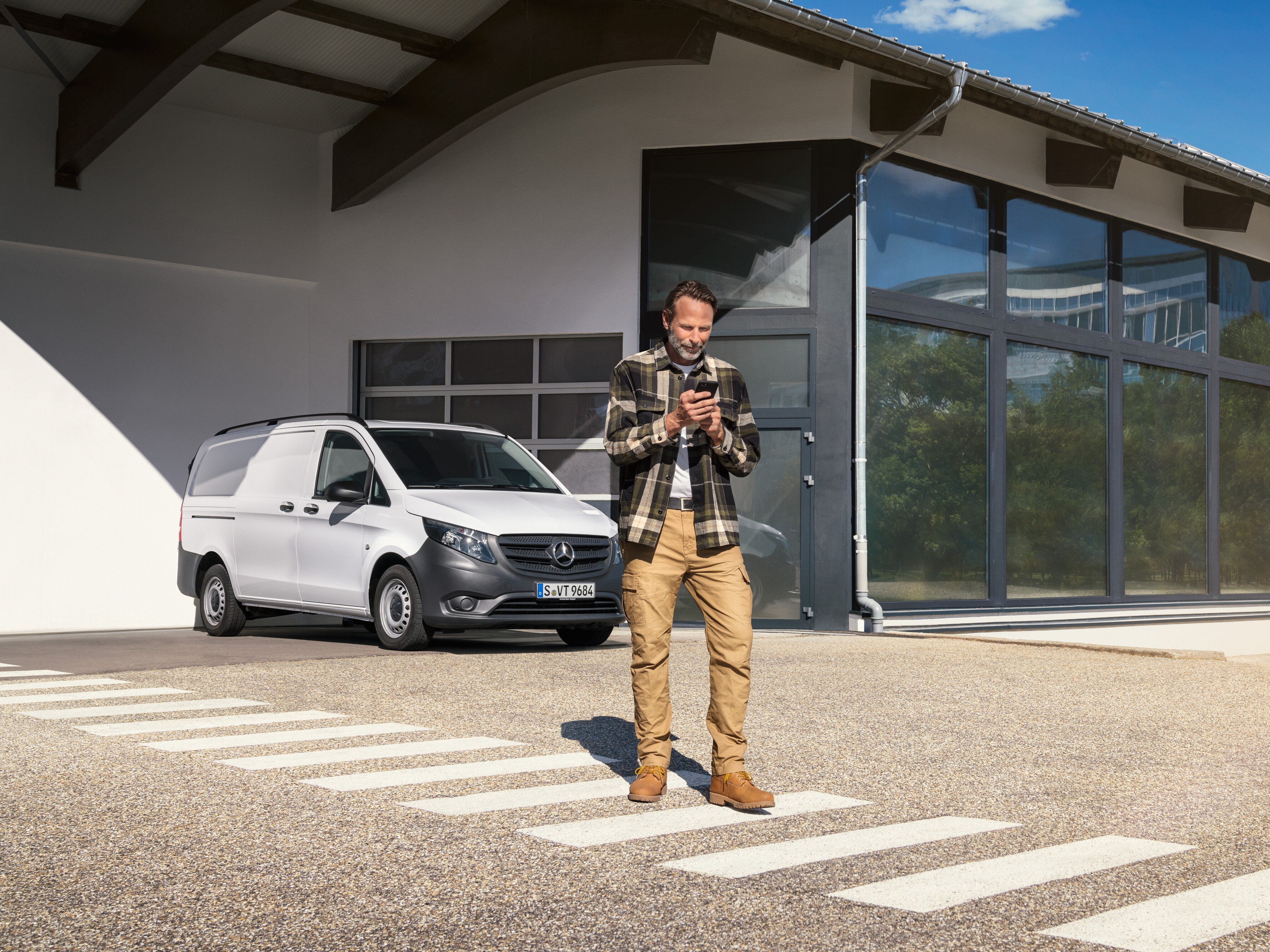 一位男士站在一輛白色 Mercedes-Benz Vito 小型商用車前使用他的智能手機。