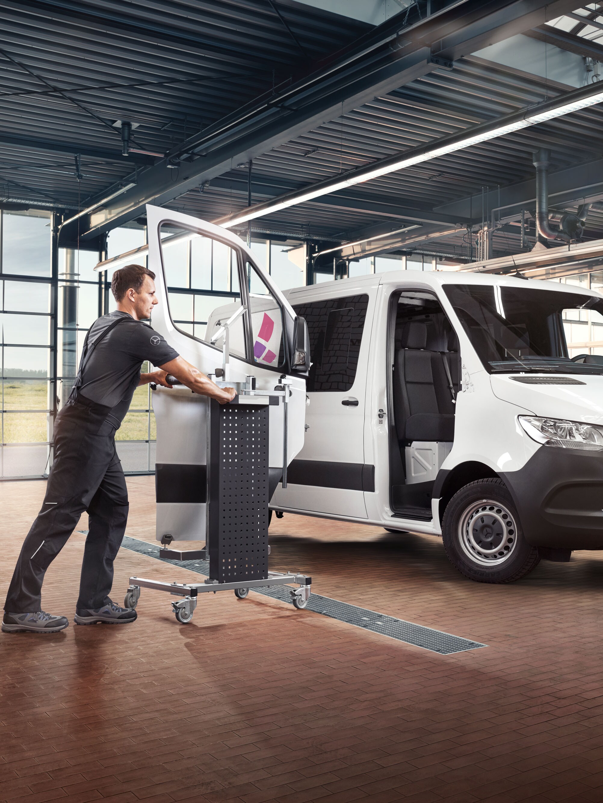 Mechanic fitting the door on a white Mercedes-benz Sprinter.